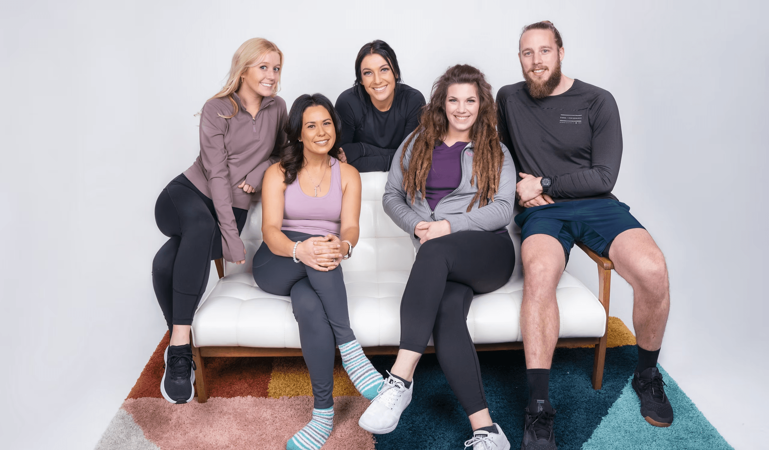 The AlignYOU team — six wellness experts seated on a white bench against a neutral studio backdrop